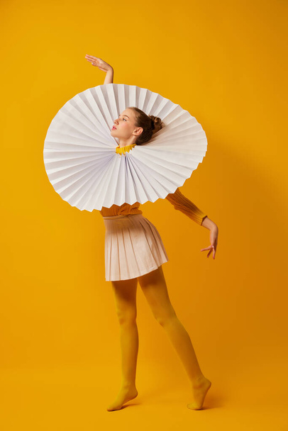 Young indifferent girl in giant jabot collar or neckwear and yellow tights dancing isolated over yellow background. Contemporary art, weird beauty, avant-garde fashion. - Photo, image