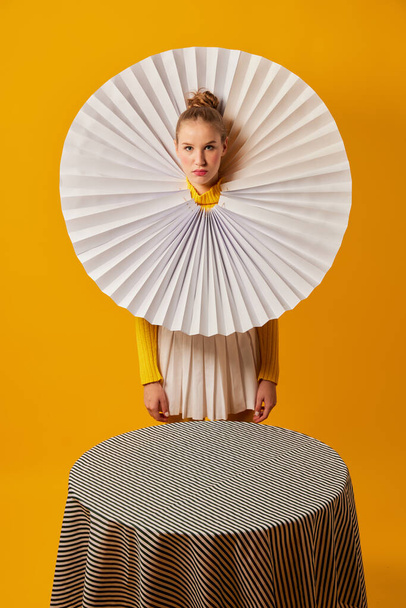 Lamp. Young indifferent girl in giant jabot collar or neckwear and yellow tights isolated over yellow background. Contemporary art, weird beauty, avant-garde fashion. - 写真・画像
