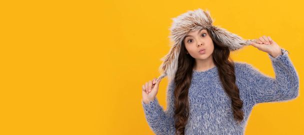 grappig kind in trui en oorflap hoed op gele achtergrond, winter. Banner van kind meisje in de winter hoed, studio poster header met kopieerruimte - Foto, afbeelding