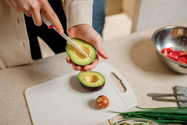 Primo piano di mani di donna che tagliano avocado fresco in cucina moderna. Nutrizione e dieta. Concetto di cibo sano. Ingredienti per frullati - Foto, immagini