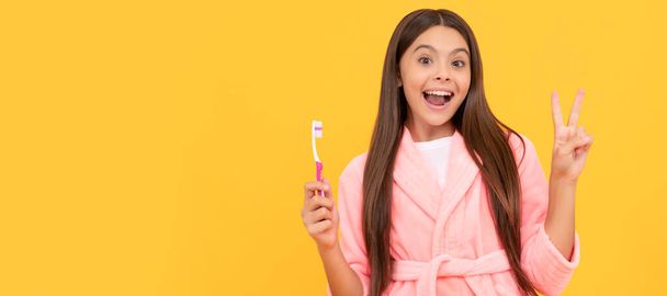 glücklich erstaunt Teenie-Mädchen im Frottee-Bademantel halten Zahnbürste zeigen Friedensgeste, Kindheit. Banner von Kindermädchen mit Zahnbürste, Studioporträt, Kopfzeile mit Kopierraum - Foto, Bild