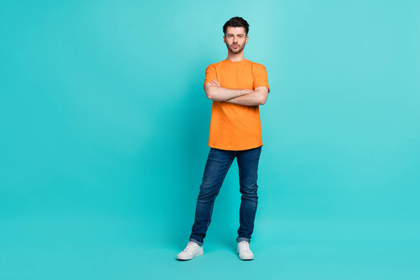 Full length photo of young handsome bearded serious man wear jeans denim orange t-shirt folded arms businessman work empty space isolated on cyan color background. - Φωτογραφία, εικόνα
