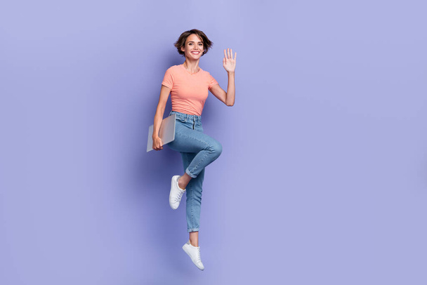 Full length photo of shiny friendly lady wear striped t-shirt jumping holding modern device waving arm empty space isolated violet color background. - Foto, immagini