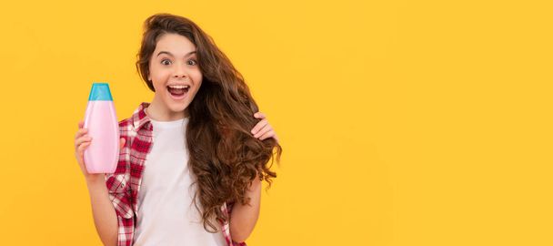 glücklich Teenager-Mädchen mit langen lockigen Haaren halten Shampoo-Flasche, Haarvolumen. Banner der Kinderhaarpflege, Plakatkopf mit Kopierraum - Foto, Bild