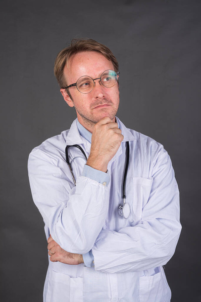 Grave medico di sesso maschile con stetoscopio sopra il collo in cappotto medico pensando e guardando verso l'alto colpo verticale - Foto, immagini