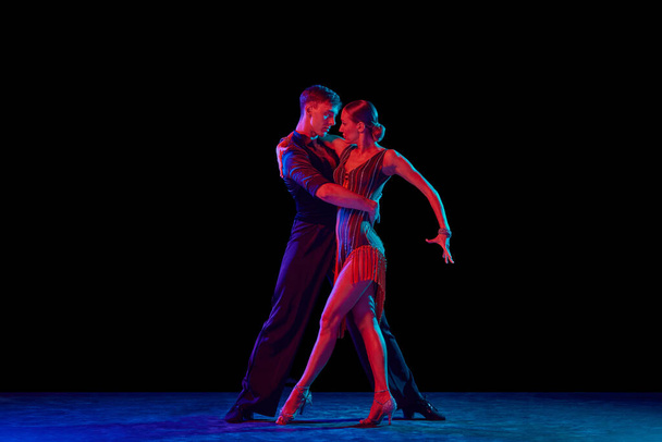 Aspiration. Stylish ballroom dancers couple in gorgeous outfits dancing in sensual pose on dark background in neon light. Concept of art, music, dance, human emotions. - Foto, Bild