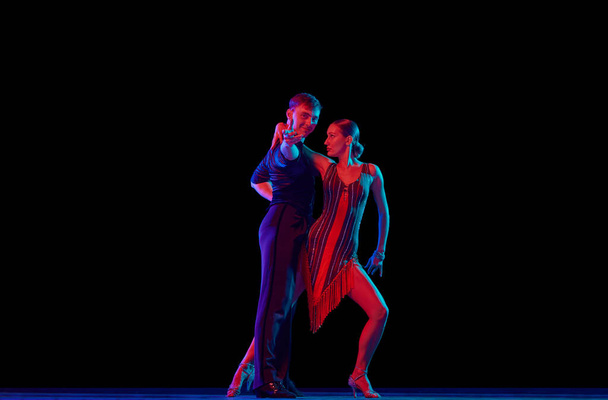 Love, hope, dreams, support. Two dancing people, ballroom dancers in elegance outfits in motion, action over dark background in neon light. Concept of art, music, dance, human emotions. - Foto, Imagem