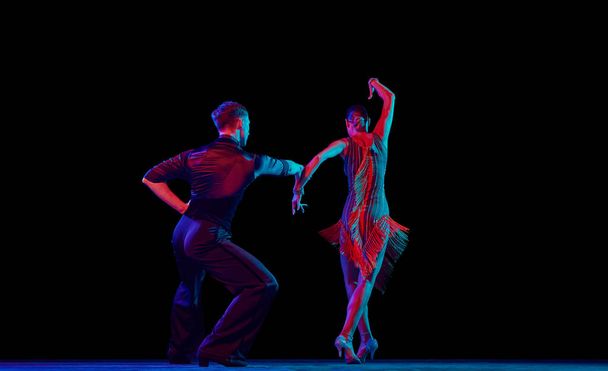 Love, hope, dreams, support. Two dancing people, ballroom dancers in elegance outfits in motion, action over dark background in neon light. Concept of art, music, dance, human emotions. - 写真・画像