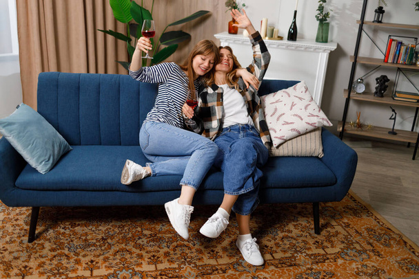 Μεθυσμένη ώριμη μητέρα και ενήλικη κόρη μιλάνε, γελάνε και αγκαλιάζονται πίνοντας κρασί στον καναπέ στο σπίτι - Φωτογραφία, εικόνα