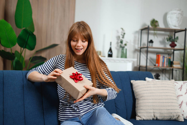 Chica sentada en el sofá en la sala de estar es feliz con su regalo de cumpleaños - Foto, imagen