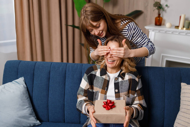 Arvaa mitä? Aikuinen tytär onnittelee onnellista kypsä äiti peittää silmänsä ja antaa lahjapakkauksen - Valokuva, kuva
