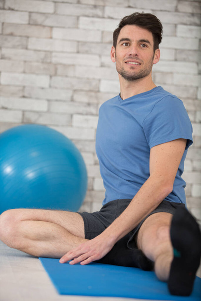 man stretching leg on yoga mat - Φωτογραφία, εικόνα
