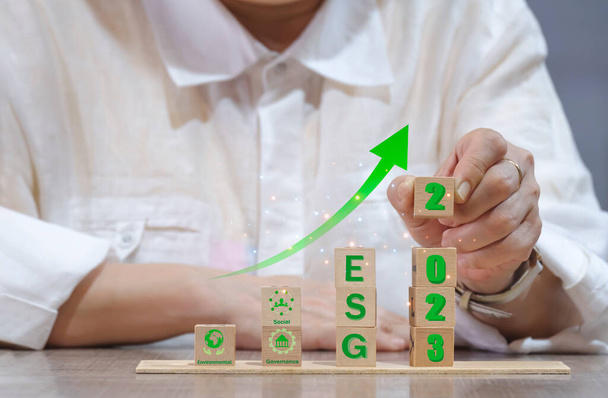Бизнесвумен, демонстрирующая разработку устойчивой бизнес-идеи 2023 года "ESG" на деревянных блоках и зеленой стрелке, указывая на свой стол, ESG концепции, экологические, социальные и управленческие - Фото, изображение