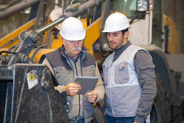 construction vehicle driver looking at tablet and discussing with foreman - Foto, afbeelding