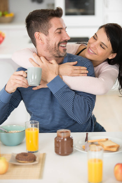 beautiful happy couple hugging during breakfast in kitchen - Foto, afbeelding
