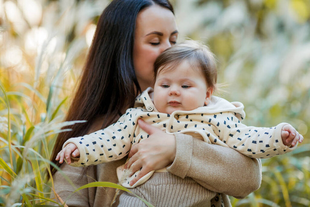 Όμορφη νεαρή μητέρα με ένα χαριτωμένο κοριτσάκι 7 μηνών βόλτες στο πάρκο του φθινοπώρου. Πορτρέτο μιας ευτυχισμένης οικογένειας. - Φωτογραφία, εικόνα