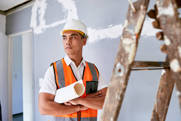 Ein seriöser Bauarbeiter steht mit Plänen unter dem Arm bei der Renovierung seines Hauses. Hochwertiges Foto - Foto, Bild