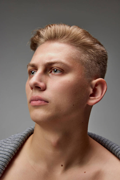 Close-up portrait of young handsome man with blonde hair looking away, posing isolated over grey studio background. Stylish haircut. Concept of mens health, natural beauty, body and skin care. - Foto, Imagen