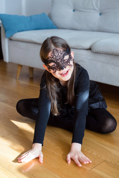 Portré egy hétéves lányról karneváli maszkban és fekete jelmezben. Közelkép. Halloween elgondolás - Fotó, kép