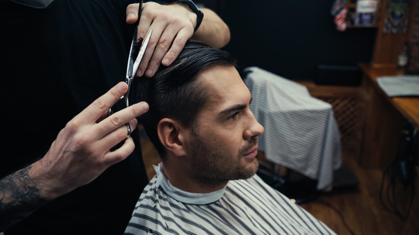 Tatoué coiffeur coupe les cheveux de l'homme en cape de coiffure dans le salon  - Photo, image