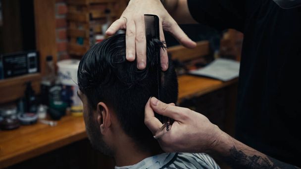 Парикмахер расчесывает волосы клиента и держит ножницы в салоне  - Фото, изображение