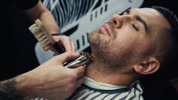 Barber trimming beard of customer in blurred barbershop  - Photo, Image