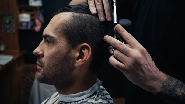 Hairdresser cutting hair of man in hairdressing cape in barbershop  - Фото, зображення