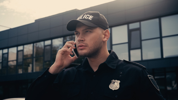 Полицейский в форме и значке разговаривает на смартфоне на городской улице   - Фото, изображение