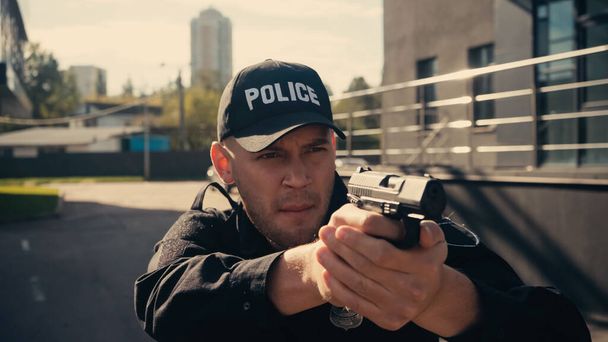 giovane poliziotto in uniforme e berretto puntando con pistola sulla strada urbana - Foto, immagini