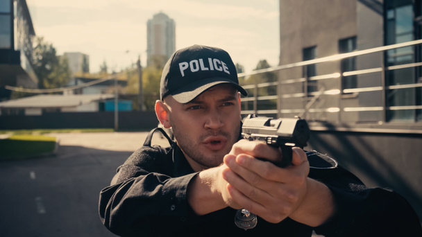 giovane poliziotto in uniforme e cap pistola in mano mentre parla sulla strada urbana  - Foto, immagini