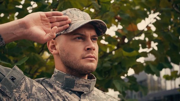 joven soldado en gorra militar y uniforme saludando al aire libre  - Foto, imagen