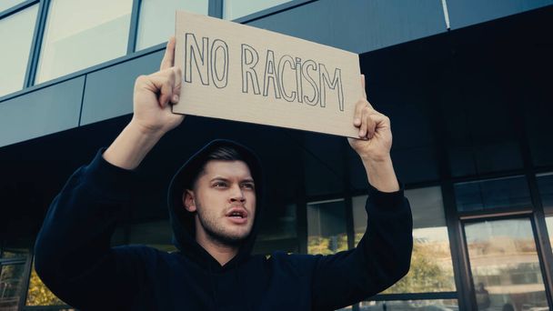 fiatal férfi kapucnis pulóver gazdaság placard nélkül rasszizmus betűk a szabadban  - Fotó, kép
