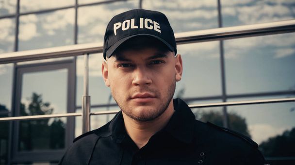 giovane poliziotto in berretto con lettering polizia e uniforme guardando la fotocamera - Foto, immagini