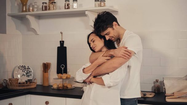 happy man with closed eyes embracing sensual girlfriend in kitchen - Photo, image