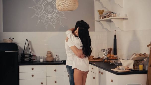 brunette young woman in white shirt embracing boyfriend in modern kitchen - Photo, Image