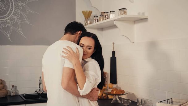 man hugging brunette and sensual woman in white shirt in kitchen  - Фото, зображення