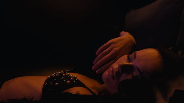 Sensual woman in bra closing eyes while lying on black background  - Фото, изображение