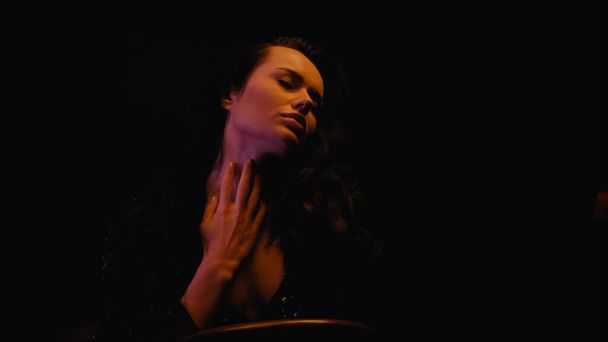 Σέξι νεαρή γυναίκα που αγγίζει το λαιμό απομονωμένη σε μαύρο  - Φωτογραφία, εικόνα