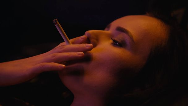 Young woman smoking cigarette isolated on black  - Foto, Bild
