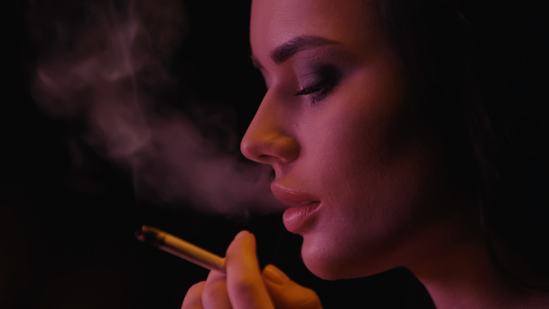 Young woman holding cigarette near smoke on black background  - Фото, зображення