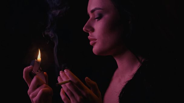 Seitenansicht der Frau mit Zigarette und Feuerzeug auf schwarzem Hintergrund  - Foto, Bild