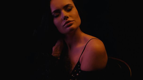 Pretty brunette woman in bra closing eyes isolated on black with lighting  - Zdjęcie, obraz