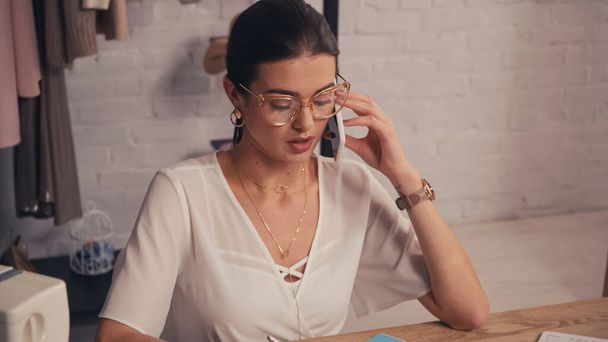 Seamstress in eyeglasses talking on smartphone in atelier  - Photo, Image