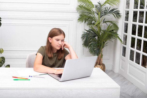Portrait d'une jolie écolière assise à la table et étudiant en ligne. Enseignement à distance et préparation au concept scolaire - Photo, image