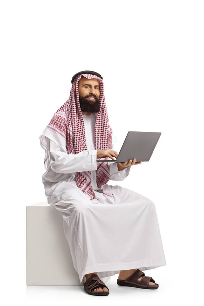 Saudi arab man with a laptop computer sitting and looking at the camera isolated on white background - Foto, imagen
