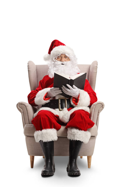 Santa claus sitting in armchair and reading a book isolated on white background - Foto, Imagen