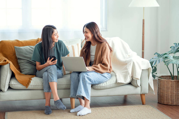 Two woman communicate with their friends and classmates via video link using a laptop and smartphone in the living room. Friends, friendship, time together - 写真・画像