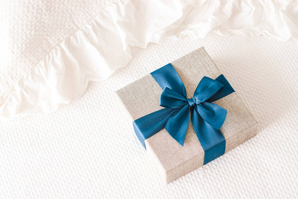 Святковий подарунок і розкішна онлайн доставка покупок, загорнута лляна подарункова коробка з синьою стрічкою на ліжку в спальні, шикарний сільський стиль, крупним планом
 - Фото, зображення