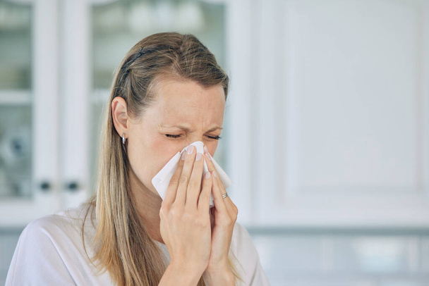 Closeup of sick caucasian woman holding tissue and blowing her nose while at home. Woman suffering from seasonal allergy or flu. - Photo, image