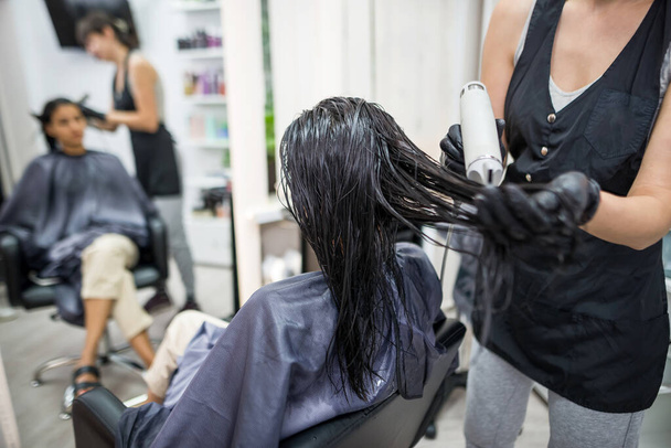 догляд за волоссям в салоні краси, жінка сидить у кріслі робить процедури з волоссям. Процес кератину для волосся. Маска, випрямлення, ламінування волосся жінок
 - Фото, зображення